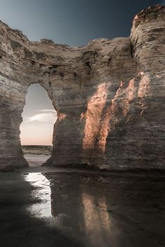 the sun is shining through an arch in the rock formation on the beach at low tide