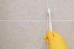 a person in yellow rubber gloves holding a toothbrush against a wall with white tiles