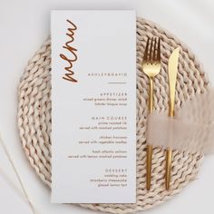 a table setting with a menu and gold utensils on top of a wicker place mat