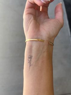 a woman's arm with a small flower tattoo on her left wrist and gold bracelet