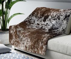 a brown and white animal print blanket sitting on top of a couch next to a potted plant