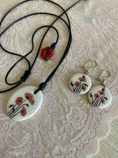 three necklaces with flowers on them sitting on a lace tablecloth next to a pair of earrings