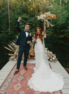 a bride and groom standing on a rug holding up their bouquets in the air