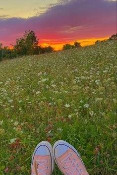 someone's feet in the grass at sunset with their shoes up on top of them