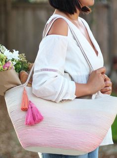 a woman carrying a large white bag with pink tassels and flowers on it