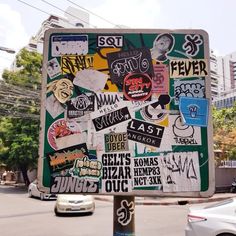 a street sign covered in stickers on the side of a road with cars passing by