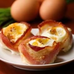 bacon wrapped eggs on a white plate with asparagus and brown eggs in the background