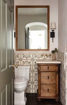 a white toilet sitting next to a wooden cabinet in a bathroom under a large mirror