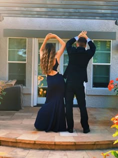 a man and woman in formal wear dancing on the front steps of a house,