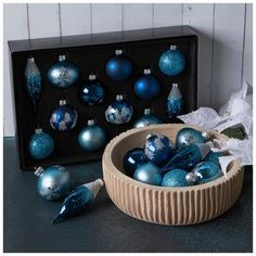 a wooden bowl filled with blue ornaments next to a black box full of christmas balls