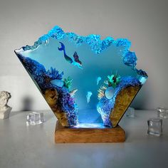 a glass bowl with an underwater scene in the center on a wooden stand next to ice cubes