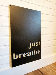 a sign that says just breathe hanging on a wall next to a wooden floor and white brick wall