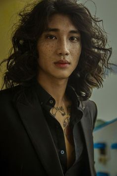 a man with long hair wearing a black suit and tattoos on his chest is looking at the camera