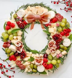 a wreath made out of cheese, grapes and meats on a white table with red berries