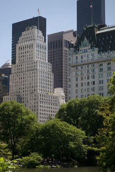 there are many tall buildings in the city with trees and water around them, as well as people walking on the sidewalk