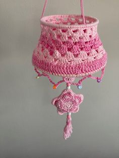 a pink crocheted basket hanging from the ceiling with tassels and beads