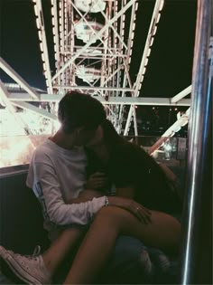 a man and woman sitting next to each other in front of a ferris wheel at night