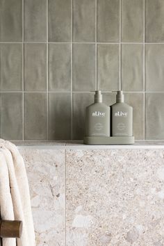 two bottles of soap sitting on top of a marble counter next to a towel rack