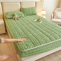 a person reaching for a bed with green bedspread and teddy bear on it