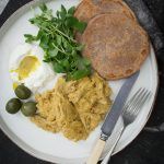 a white plate topped with eggs, bread and vegetables next to a fork and knife