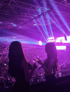 two women standing in front of a crowd at a concert with bright lights on the stage