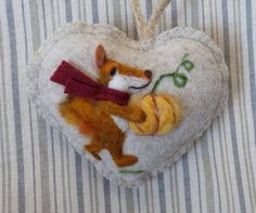 a felt ornament shaped like a heart with a squirrel holding a tennis ball