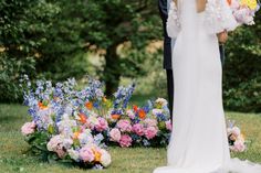 a bride and groom standing next to each other in front of colorful flowers on the grass