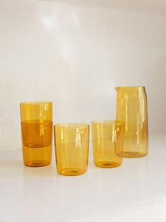 three yellow glass cups sitting next to each other on a white counter top in front of a white wall