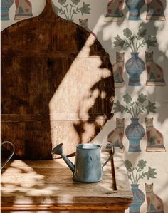 a wooden table topped with a watering can next to a wall covered in vases