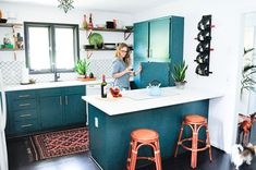 a woman standing in a kitchen with two stools next to a counter and an island