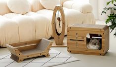 a cat sitting in a wooden box next to a couch and table with pillows on it