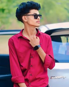 a young man wearing sunglasses standing in front of a car with his hand under his chin