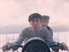 two men riding on the back of a motorcycle in snow covered mountains behind them,