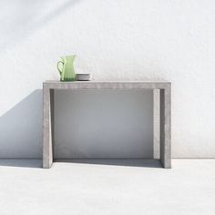 an empty concrete table with a green vase on top and plates in the middle, against a white wall