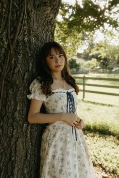 a woman in a dress leaning against a tree