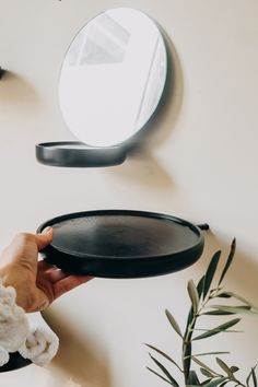 a person holding a black plate in front of a round mirror on a white wall