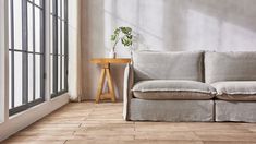 a white couch sitting in front of a window next to a wooden table with a potted plant on it