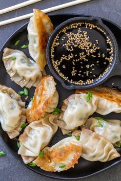 a black plate topped with dumplings next to a bowl of sauce and chopsticks