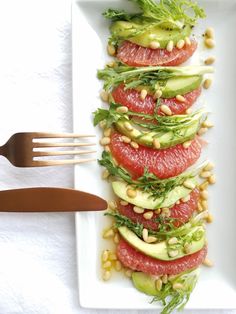 a white plate topped with slices of grapefruit and avocado next to a fork