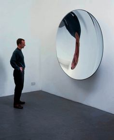 a man standing in front of a round mirror on the wall next to another person