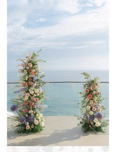 two tall floral arrangements sitting next to each other on top of a building near the ocean