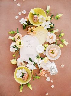 an arrangement of flowers, candles and other items on a pink surface with petals scattered around it