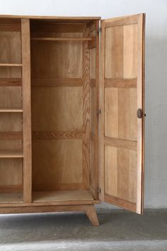 an open wooden cabinet sitting on top of a cement floor next to a white wall