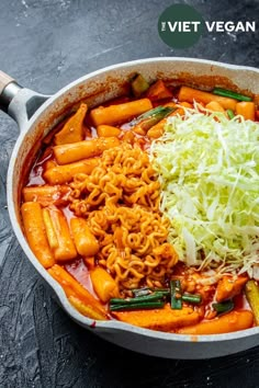 a pot filled with pasta and vegetables on top of a black table next to a wooden spoon