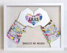 a white frame with colorful bracelets and a heart shaped paper cutout in the middle