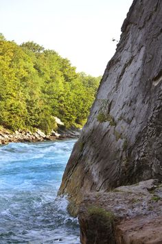 the water is blue and green as it flows between two large rocks in front of some trees