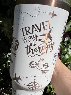 a person holding up a travel mug with stickers on it's side in front of some bushes