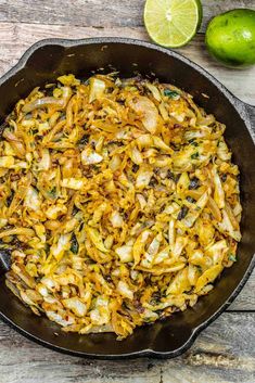 a skillet filled with rice and vegetables on top of a wooden table next to limes