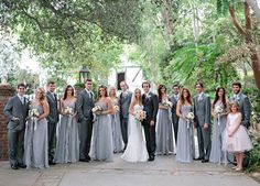 a group of people standing next to each other in front of trees and bushes at a wedding