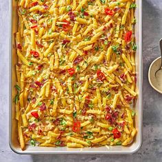 a casserole dish filled with pasta, cheese and vegetables next to a spoon